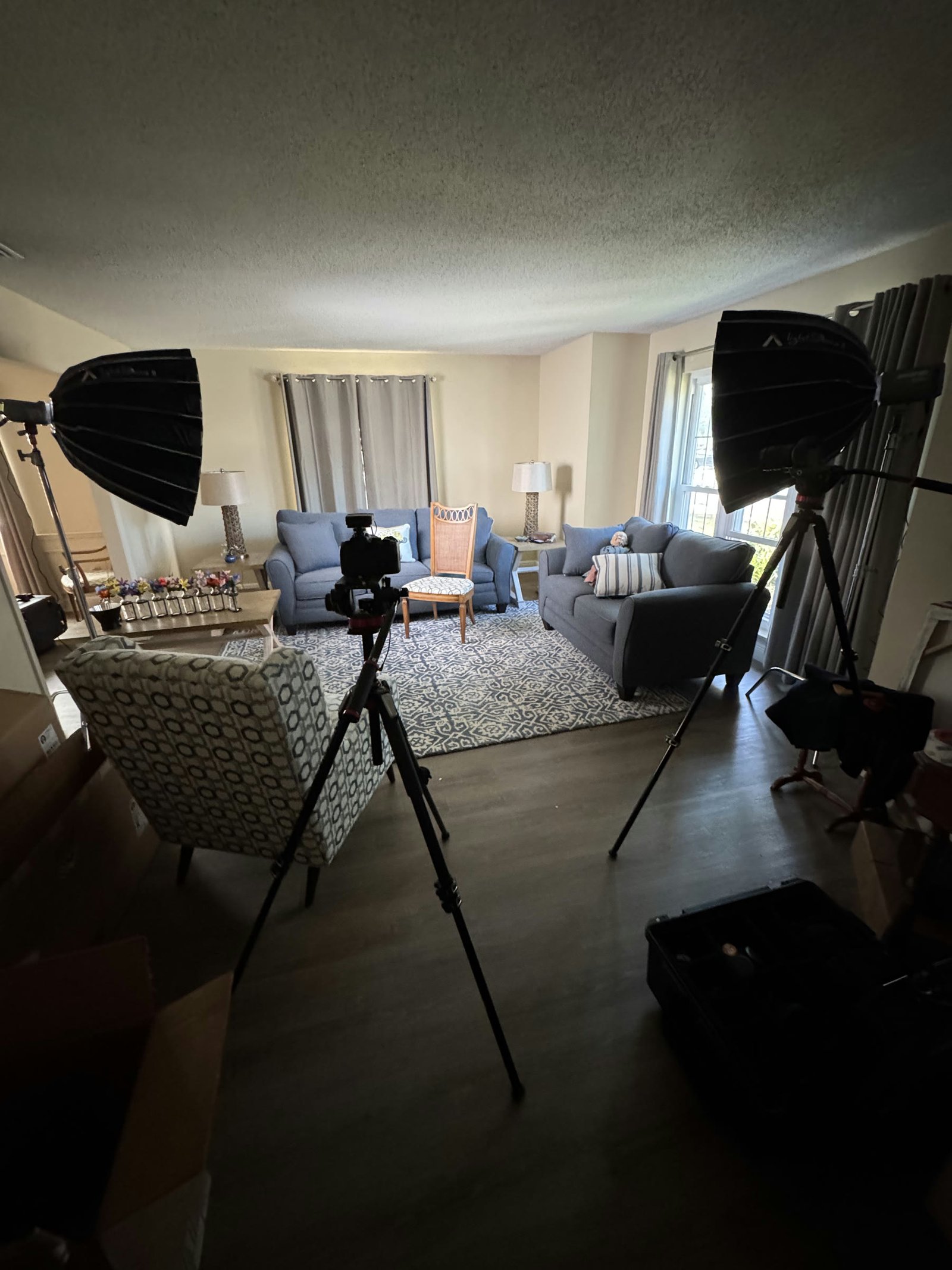 A documentary interview setup inside a living room, with softbox lights and cameras framing the seating area.